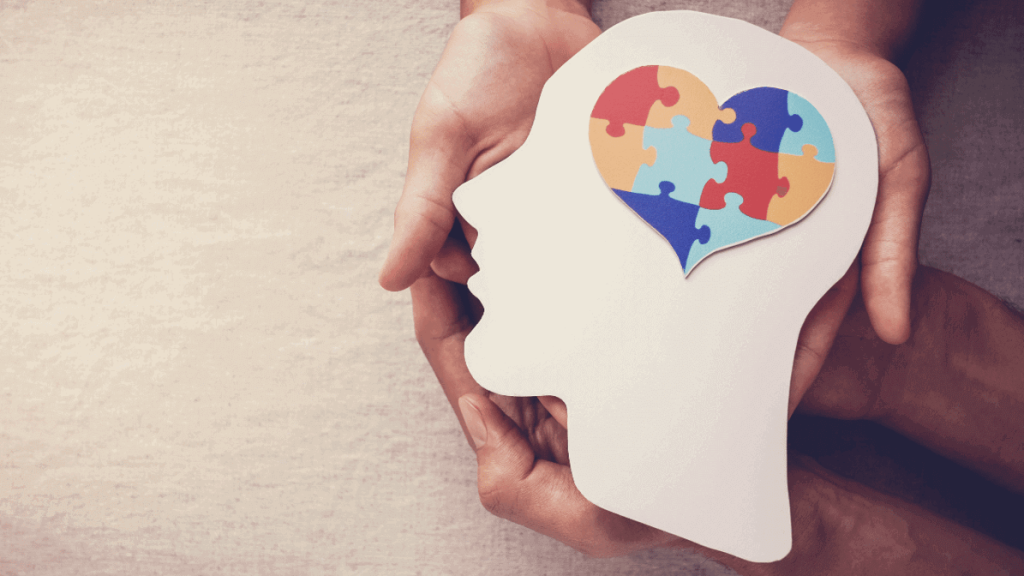 people holding a paper cutout of a person's face silhouette and a heart made up of puzzle pieces on top