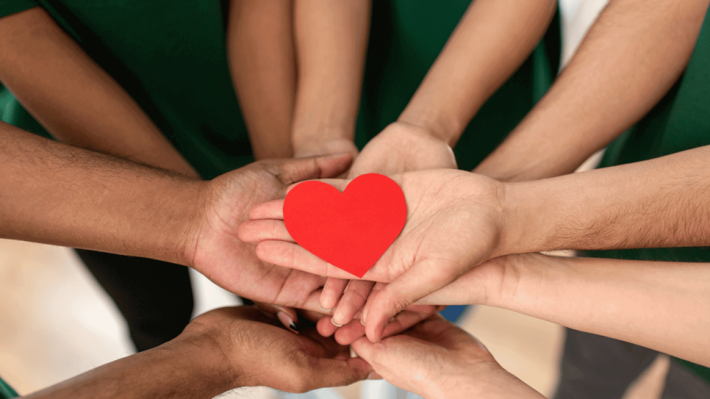 multiple volunteers' hands holding a paper heart